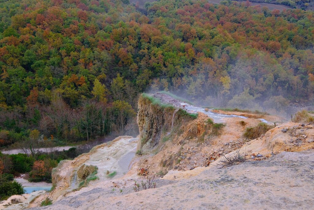 Steaming thermal water running over the travertine cliff of the Parco dei Mulini, Bagno Vignoni, among autumn trees