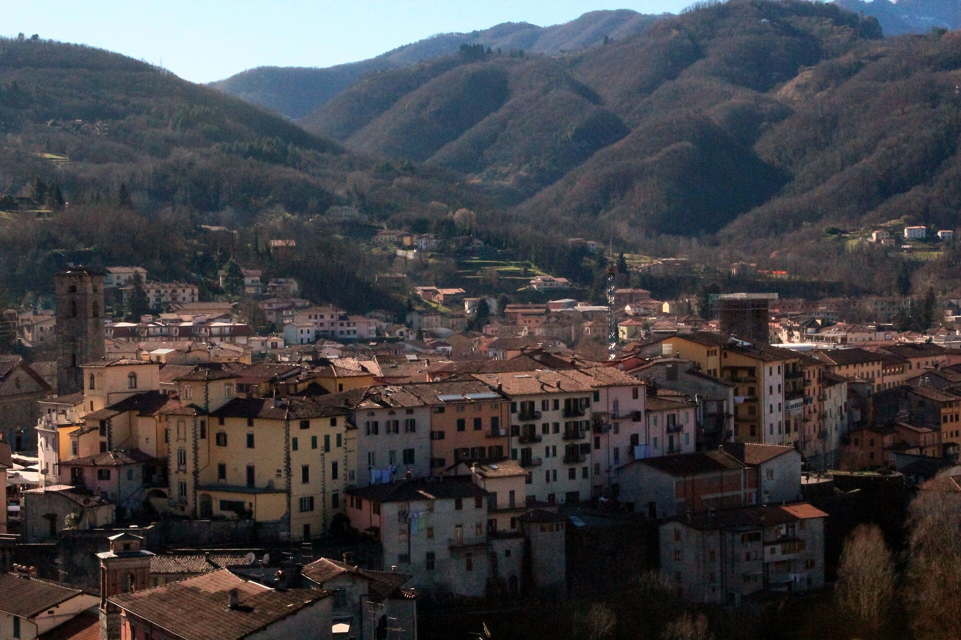 Ochre and terracotta houses of Castelnuovo di Garfagnana with a bell tower, backed by wooded mountains