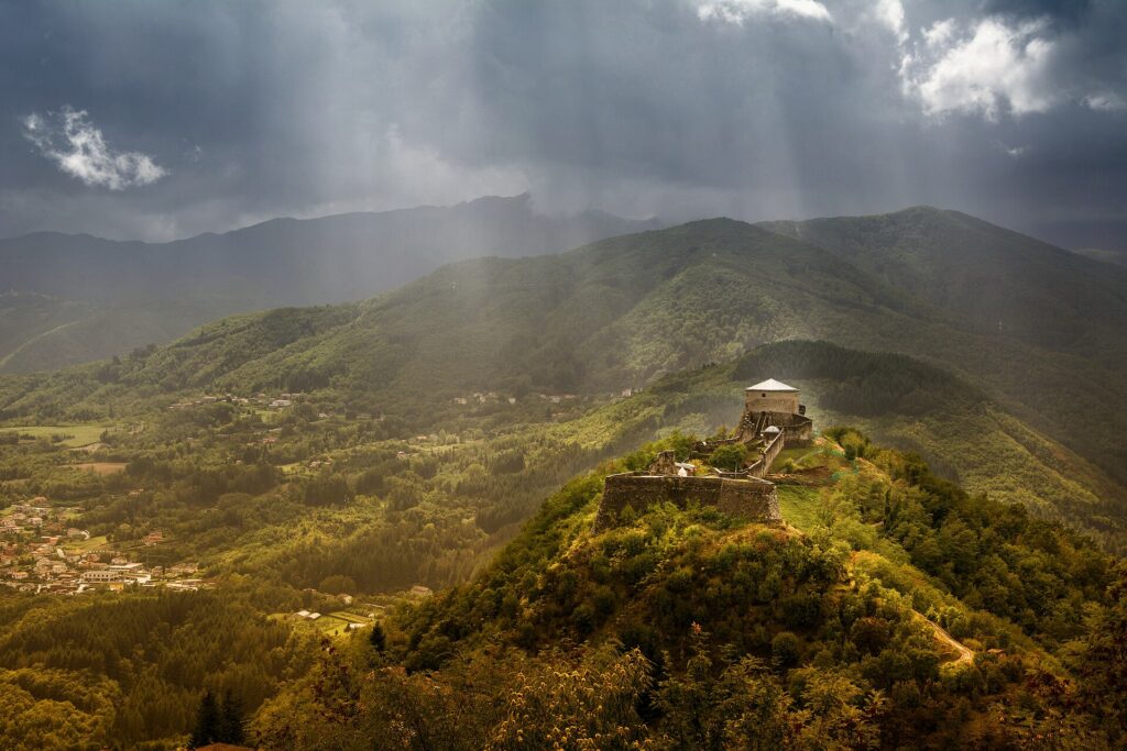 Sunbeams lighting the Fortezza delle Verrucole on its wooded hilltop above the Garfagnana valley