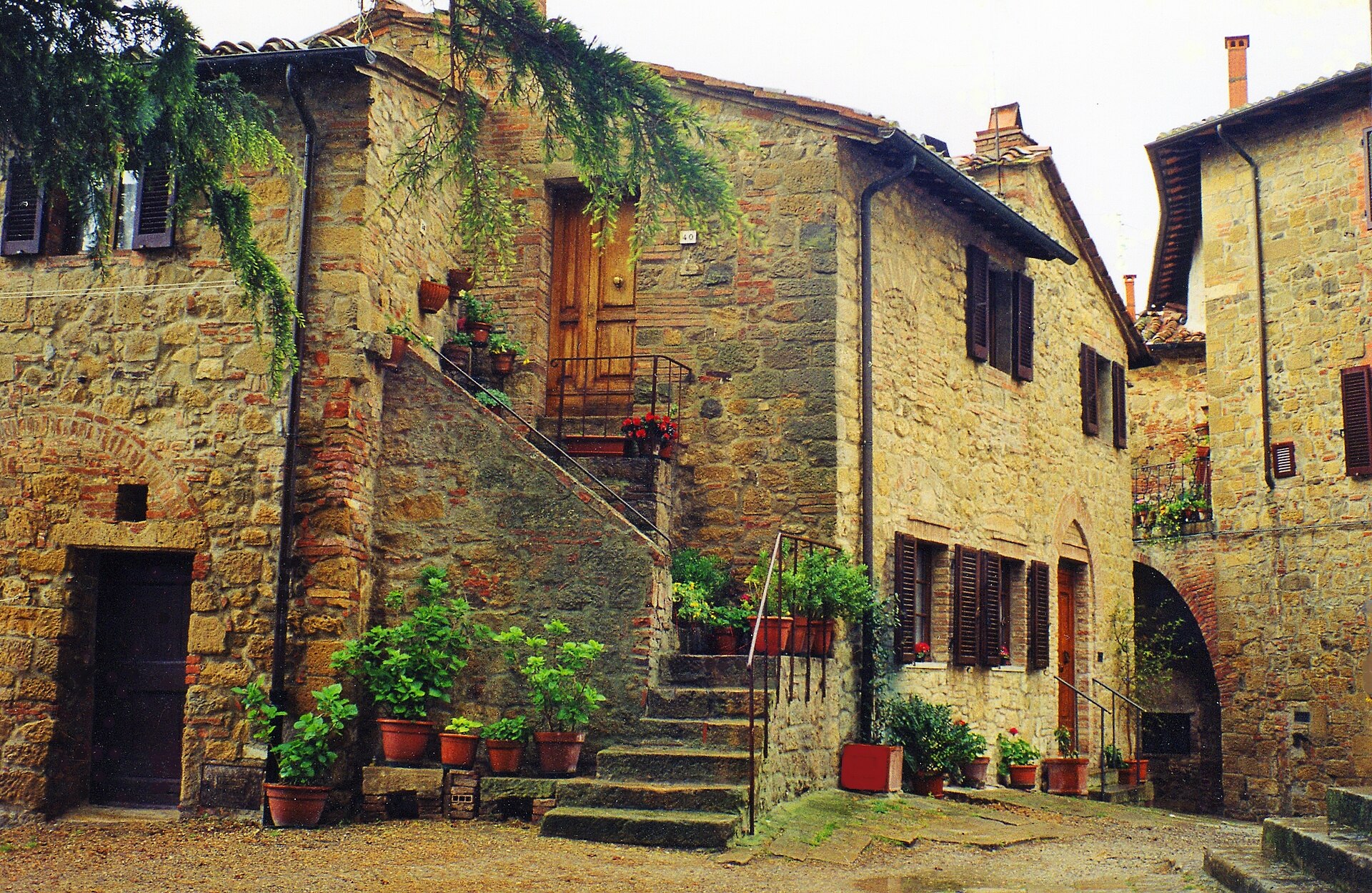 Stone houses and an outdoor stair lined with potted flowers inside the walls of Monticchiello