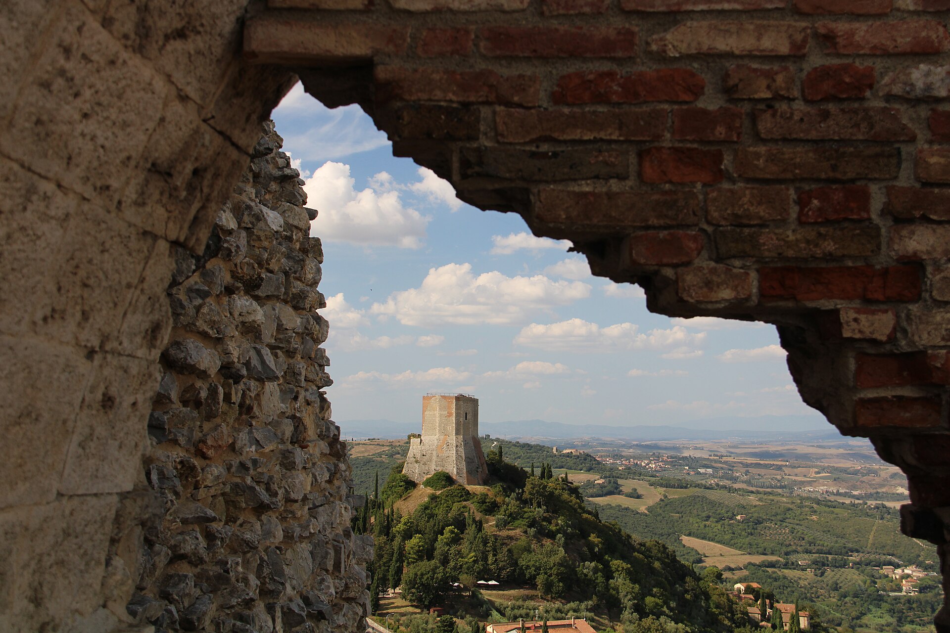 The Val d'Orcia seen through a ruined brick arch at Rocca a Tentennano, with a tower on the hill beyond