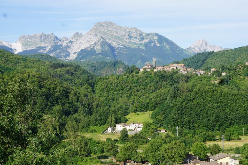 Green wooded valley at Piazza al Serchio with a hilltop village and the pale peaks of the Apuan Alps beyond