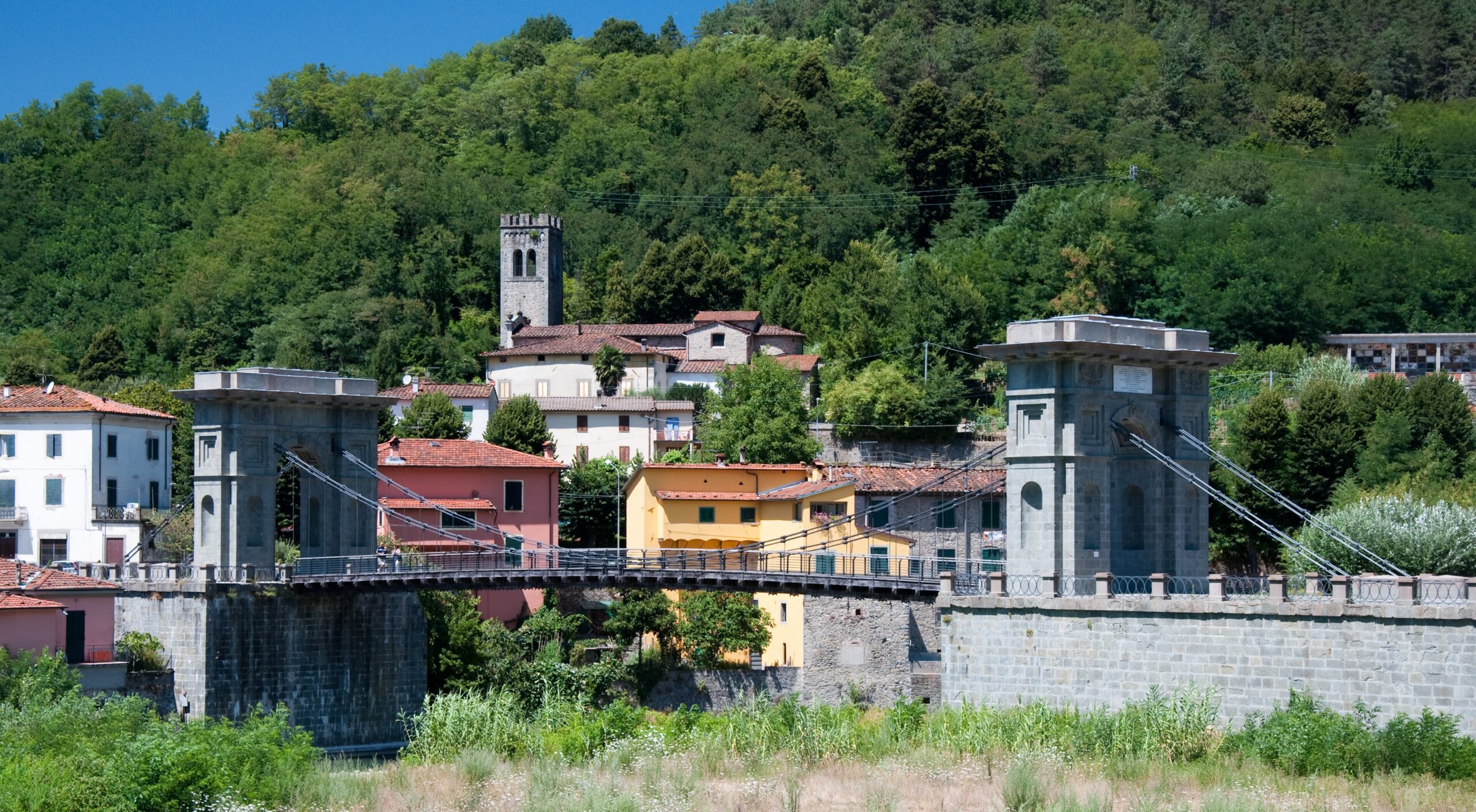 Ponte delle Catene chain bridge with stone gate towers at Fornoli, Bagni di Lucca, colourful houses and wooded hill behind