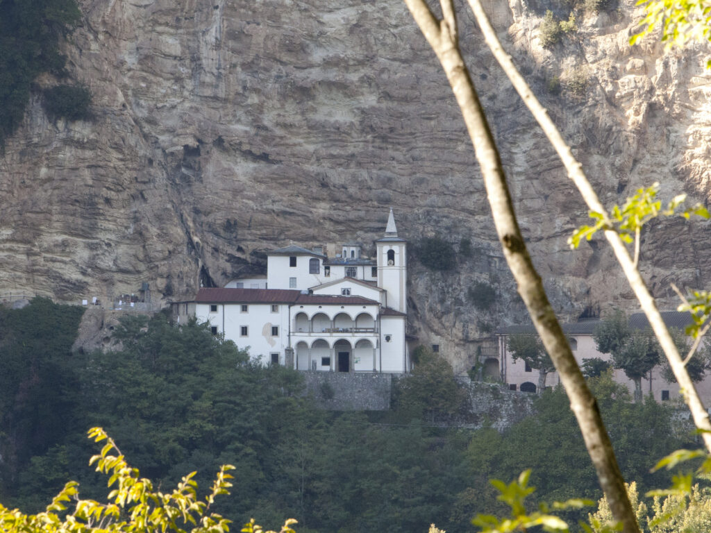 The white Eremo di Calomini hermitage built against a sheer ochre limestone cliff above wooded slopes