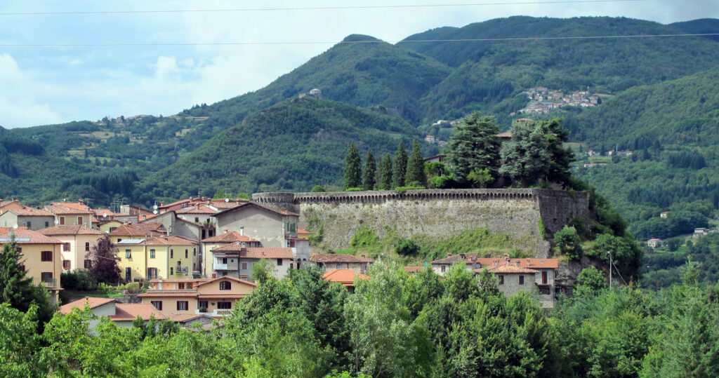 The stone walls of the Rocca Estense above Camporgiano's terracotta-roofed houses, with wooded Garfagnana hills behind