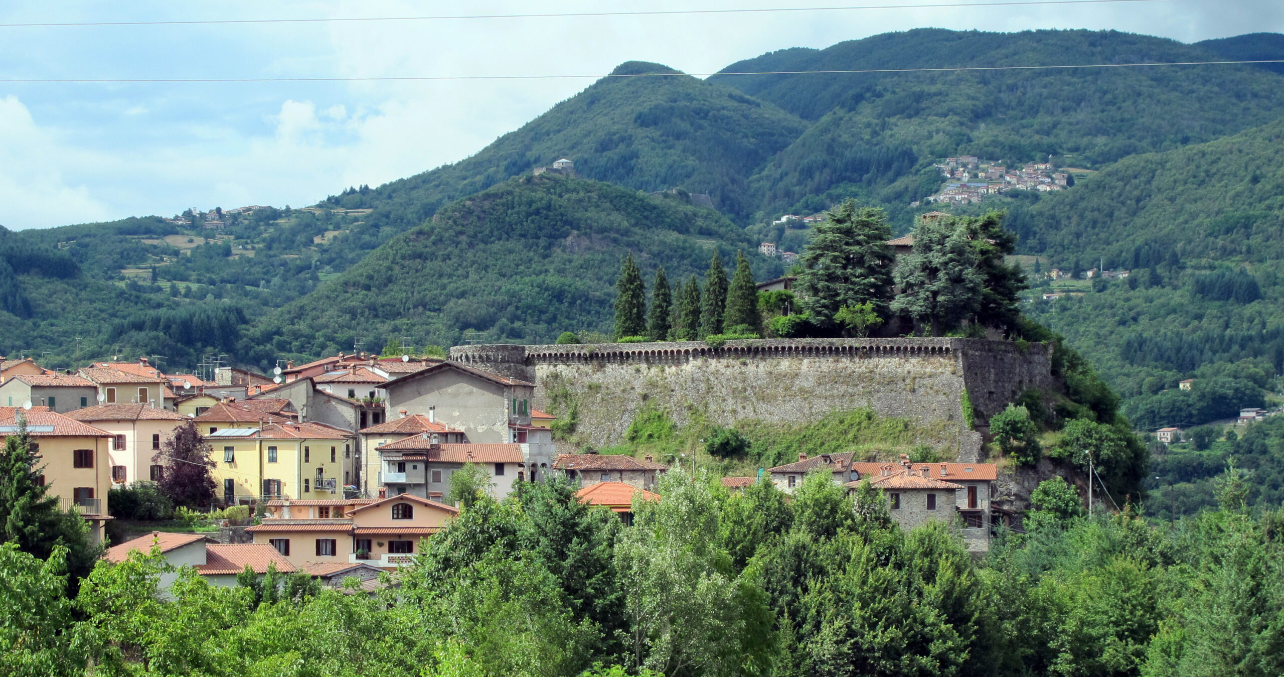 The stone walls of the Rocca Estense above Camporgiano's terracotta-roofed houses, with wooded Garfagnana hills behind